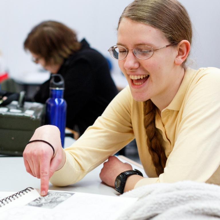 A smiling student points at a notebook during a class discussion